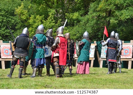 medieval knights in armor stand near the stands for archery