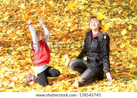 Mom and daughter throw each other yellow maple leaves