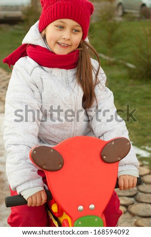little girl sits on a wooden toy motorbike