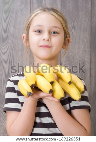 little girl holding a bunch of bananas on the background of wooden boards