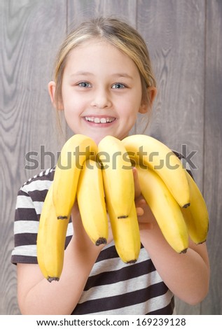 smiling girl holding a bunch of bananas on the background of wooden boards