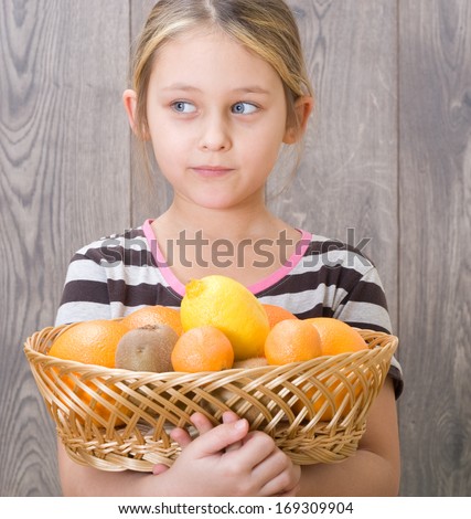 little girl holding a basket of fruit on the background of wooden boards
