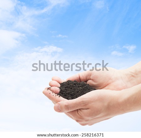 ground in human palms on blue sky background