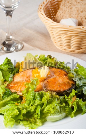 fried salmon on a garden salad topped with fresh butter and bread on a side