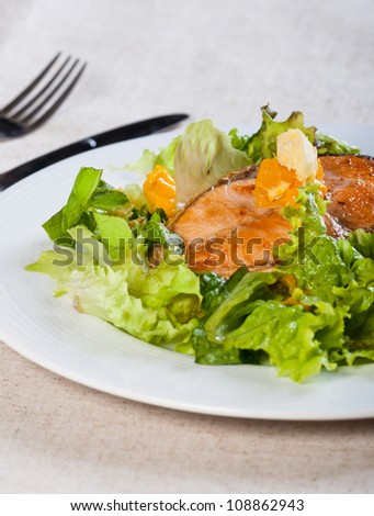 fried salmon on a garden salad topped with fresh butter