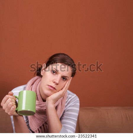 A young sick woman with a cup of tea in her hand. She hold her head in pain. A lot of copyspace.