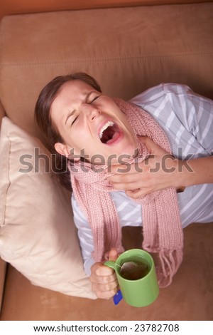 A young woman is sick. She is lying on the couch, sneezing. She has a tea in her hand.