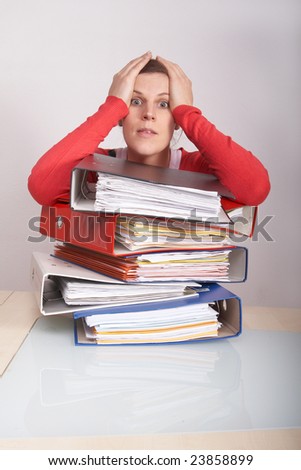 A young and beautiful female worker is stressed with a lot of paperwork in front of her. A lot of copyspace.