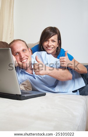 Young couple on the couch at home looking at the laptop! They both give a thumbs up sign!