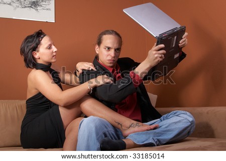Young couple on the couch surfing the web with their laptop. The man is angry with the laptop.