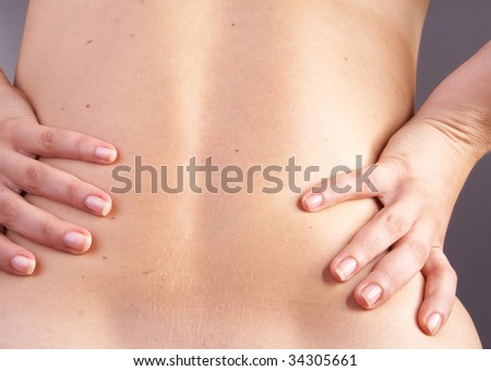 Young woman with sever back pain. She is holding her schoulder. Over gray background.