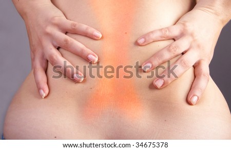 Young woman with sever back pain. She is holding her schoulder. Over gray background. The hurting area was saturated in red to symbolize the pain.