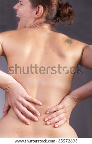 Young woman with sever back pain. She is holding her schoulder. Over gray background.