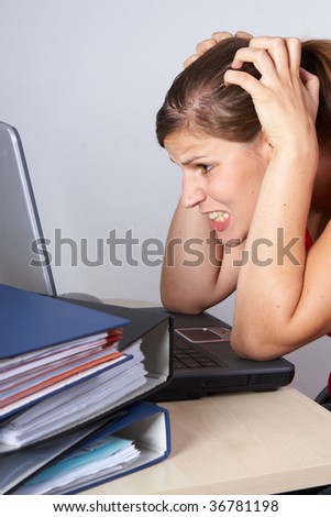 Young woman sitting at her laptop with a lot of work in front of her. She is very frustrated.