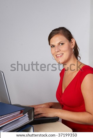 Young woman is sitting in front of her laptop and a lot of work in front of her.