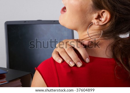 Young woman sitting at her laptop with a lot of work in front of her. She has a pain in her neck / back.