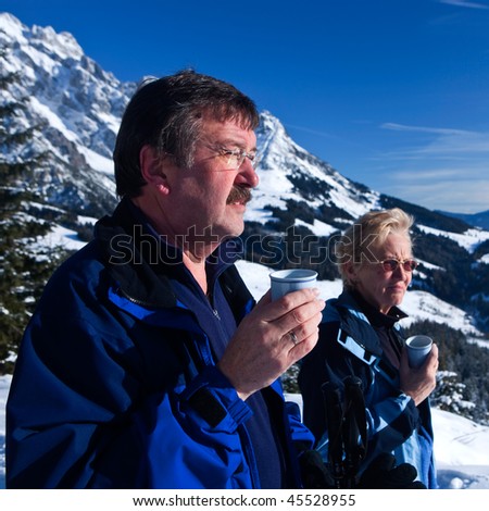 A senior couple in a winter setting in the alpine mountains. Active and happy seniors.They are having a cup of tea.
