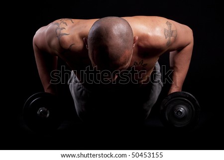 Young bald strong man is working out over black background.