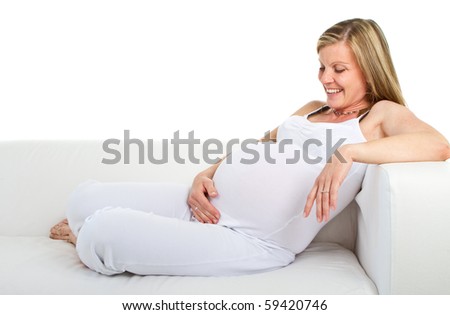 Young fresh pregnant woman lying on a stylish white couch over white background.