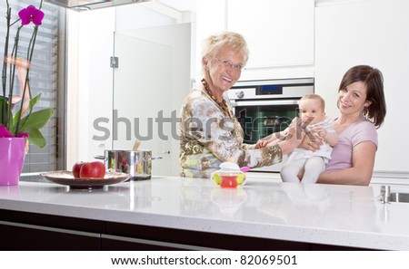 Young mother with baby girl and the grandmother in a modern kitchen setting.