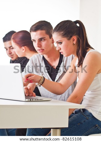 Young couple in front of laptop with others in the background. Candid picture.