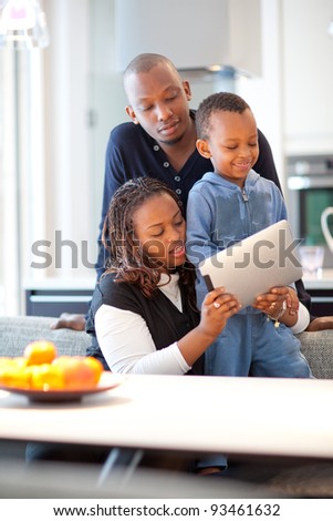 Kitchen setting with young black family playing with a tablet pc.