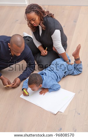 Young black family sitting on the floor drawing a picture with their son.