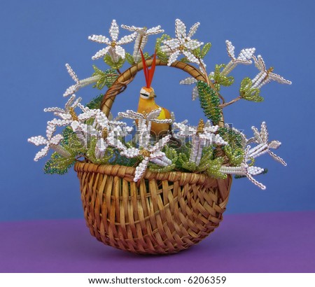 The basket decorated by beads. Flowers are made of beads. The bird in the middle sits.