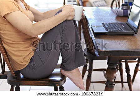 Young adult sitting at table with mug and laptop