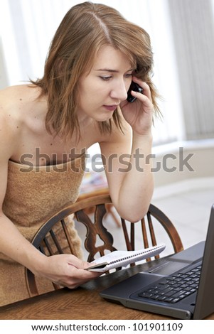 Young lady covered with brown bath towel while reading brief notes in front of laptop