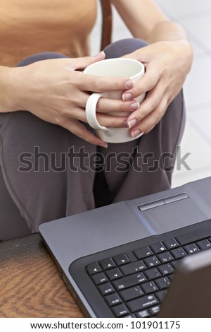 Hands holding white mug in front of laptop