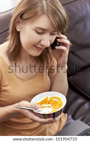 Young lady chatting on cellphone and holding a bowl of healthy food