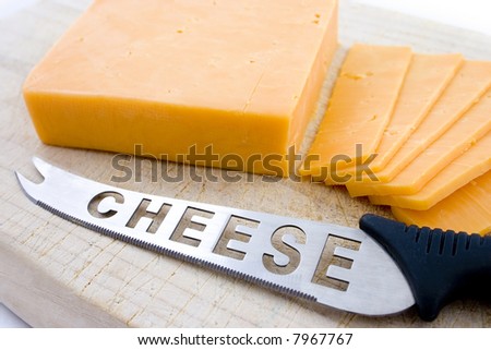 Yellow cheese sliced on top of wooden board with sharp knife