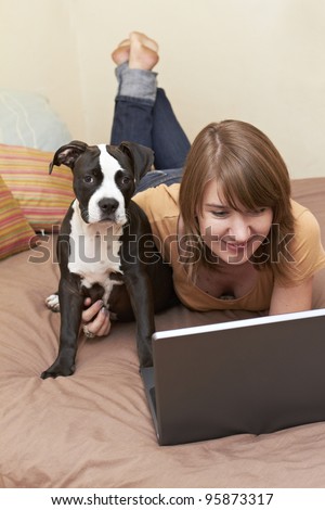 Pit Bull puppy sitting on bed with female owner looking at laptop