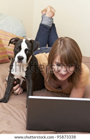 Young adult lady with her Pit Bull puppy staring at laptop