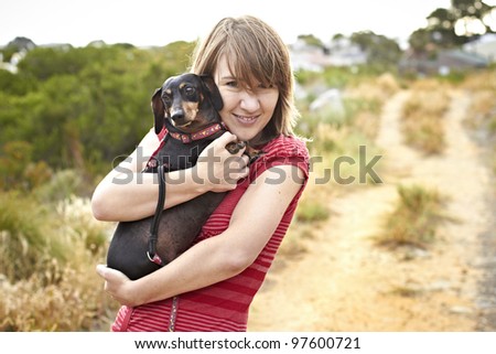 Black Dachshund dog being hugged by young lady dressed in short red summer shirt