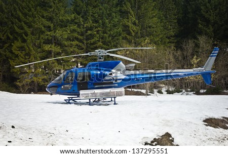 blue helicopter resting on the snow near a wood
