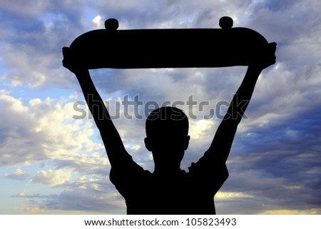 Youth boy expressing himself with raised skateboard gesture while looking at a very vivid sky with striking cloud formation (silhouette).