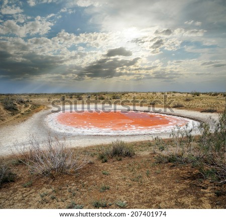 small red round lake with red iron compounds in water dries up in the dry semi-desert steppe with salt residues along the coast
