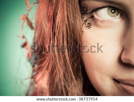 Half face portrait of a young happy woman with art fairy makeup and leaves in hair