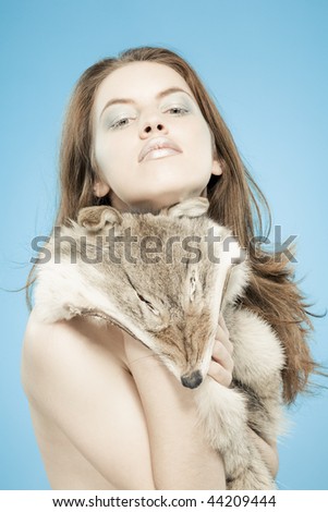 Fashion exotic portrait: young attractive shirtless girl with wolf`s fell looking to camera. Woman on blue background