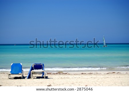 caribbean beach with a recreation sailing boat and two chairs in the first plan