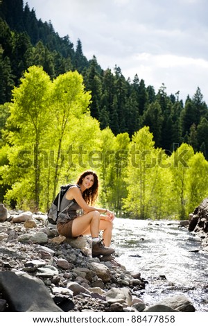 attractive young woman sitting by a mountain stream