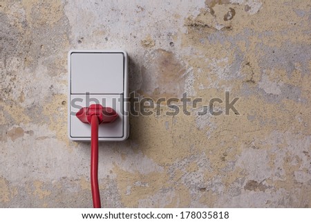 Red chord and plug in a white electrical socket on a worn brick wall