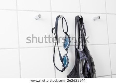 Swimming goggles and bathing suit hanging on tile wall