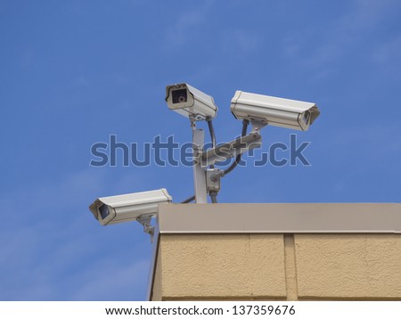 Three security cameras on a building against blue sky