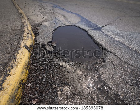 Large deep pothole as an example of poor road maintenance due to cutbacks on the infrastructure budget