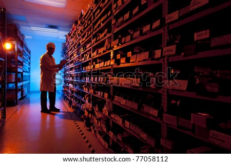 Worker checking inventory in stock room of a manufacturing company, backlit by blue and orange lighting