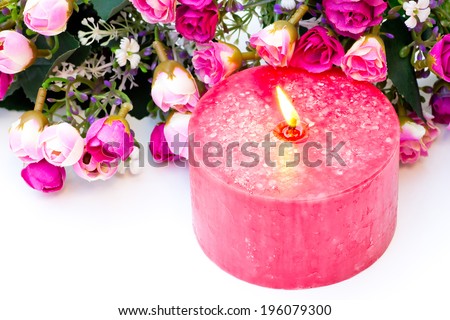 Closeup studio shot of a candle with flame and fabric roses on white background.