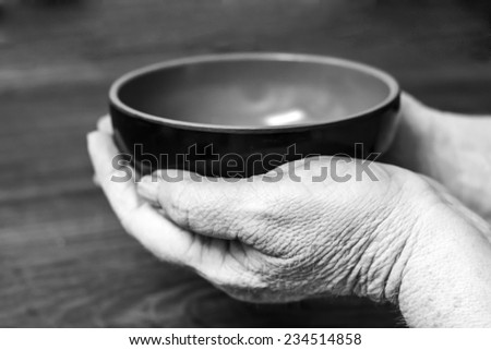 Closeup of old hands holding a cooking pot, edited in black and white
